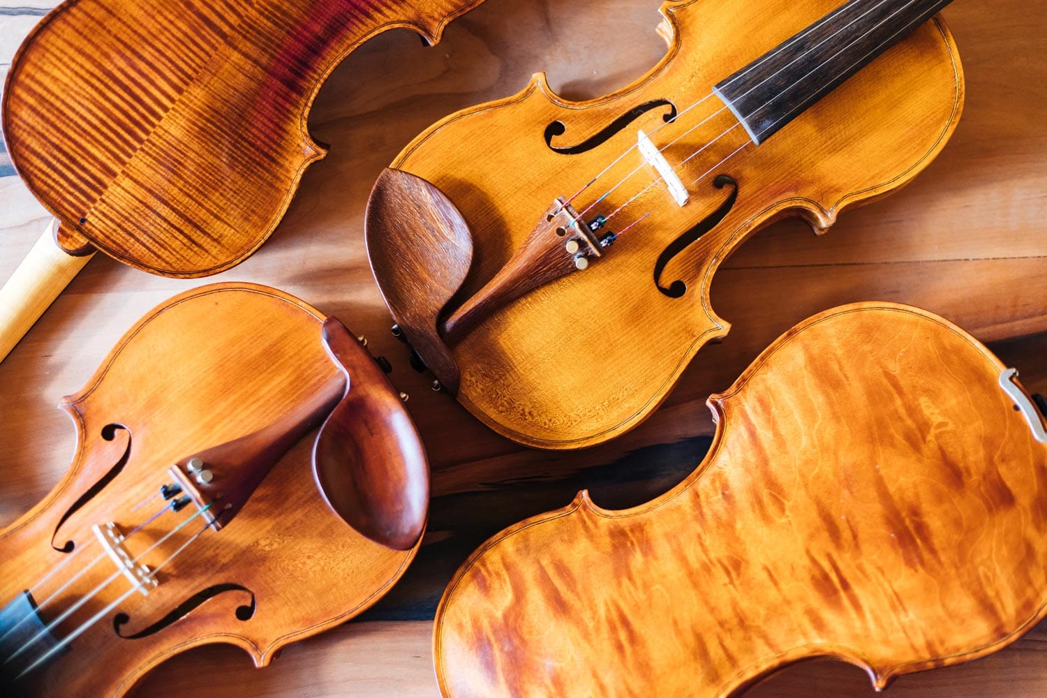 Four handmade violins with maple backs and spruce tops, photographed from above in Elvedin Hodžić's workshop